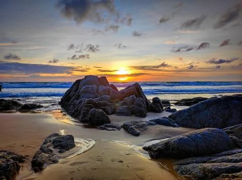 Sunset over the ocean with rocks on the beach at a coastal area Stock Photos