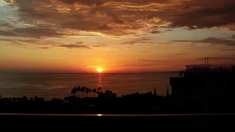 Sunset over ocean, town and railing in foreground, orange clouds Stock Footage 77973974
