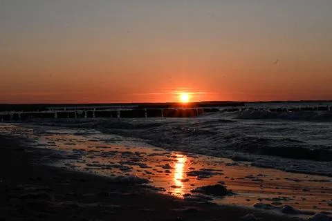 Sunset over the ocean with waves and a pier in the background during the ev.. Stock Photos