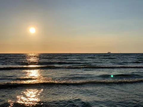 Sunset over the ocean with waves and a boat in the distance Stock Photos