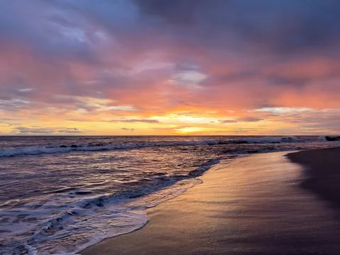 Sunset over the ocean with waves and clouds at a beach 스톡 사진