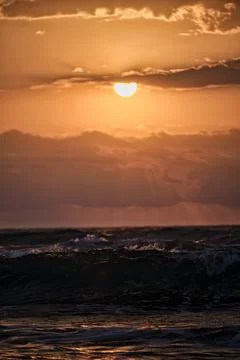 Sunset over ocean waves with clouds in sky and a warm glow reflecting on wa.. Stock Photos