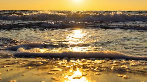Sunset over the ocean with waves crashing and light reflecting on the water's Stock Photos
