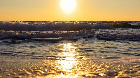 Sunset over the ocean with waves crashing on the shore during the evening Stock Photos