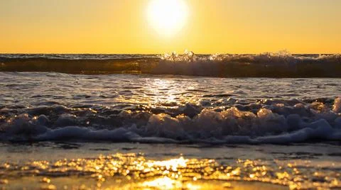Sunset over the ocean with waves crashing on the shore during golden hour in a Stock Photos