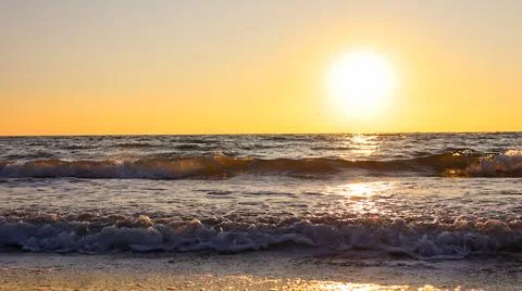 Sunset over the ocean with waves gently crashing on the shore in a coastal Stock Photos