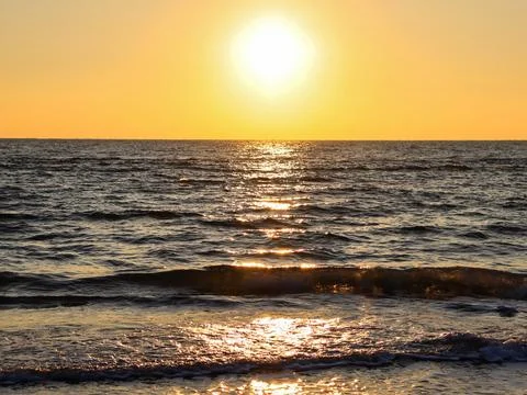 Sunset over the ocean with waves gently rolling on the shore in a calm evening 库存照片