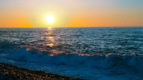 Sunset over ocean waves with pebbled beach in foreground Stock Photos