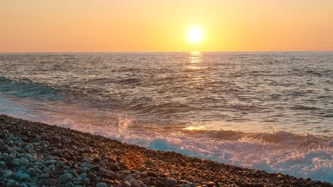 Sunset over ocean waves with pebbled beach in foreground Stock Photos