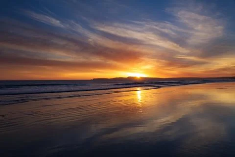 Sunset Over Ocean Waves Reflected In Wet Sandy Beach Stock Photos