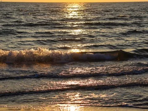 Sunset over the ocean waves with reflection on water and light from the sun Stock Photos