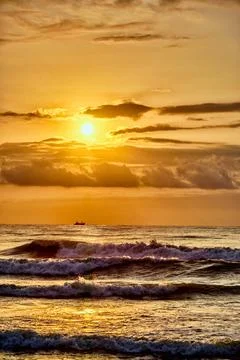 Sunset over ocean waves with small boat in distance on a clear evening Foto stock