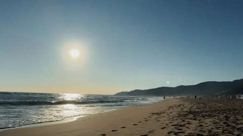 Sunset over ocean waves washing the beach sand on mountain silhouette background Stock Footage 309378742