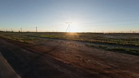 Sunset over open field with power lines and wind turbines in the distance Video stock 342230630