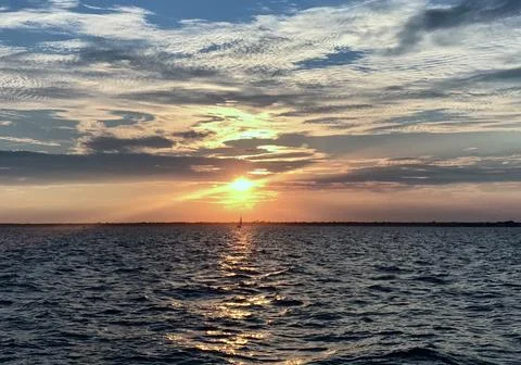 Sunset Over Open Water And A Sailboat In The Distance Stock Photos