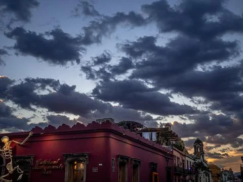 Sunset over a red building on which a skeleton is climbing Stock Photos