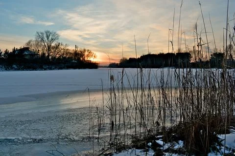 Sunset over a river covered in ice and snow. Reeds in the foreground. Foto stock
