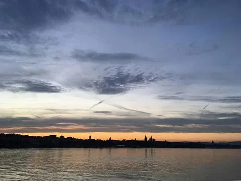Sunset over river with dramatic clouds and city skyline Stock Photos