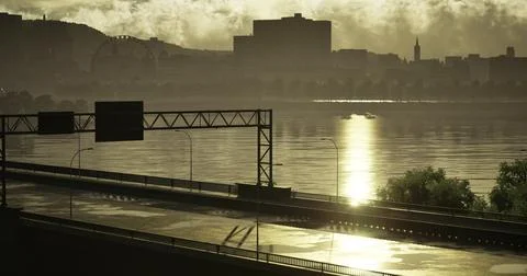 Sunset over river reflects city skyline and empty highway Ilustração Stock