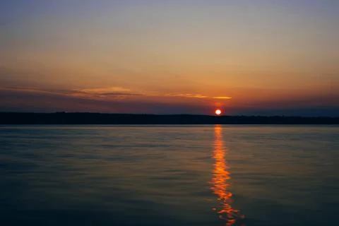 Sunset over river with sun and silhouette of the shore on warm summer evening Stock Photos