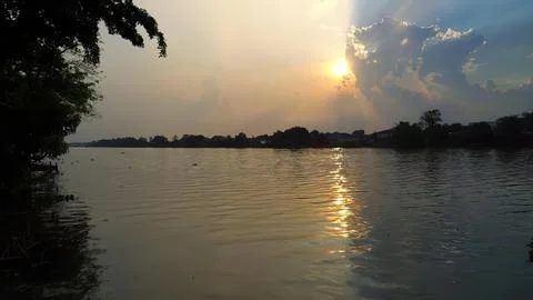 Sunset over river with trees and cloudy sky in the evening Stock Photos