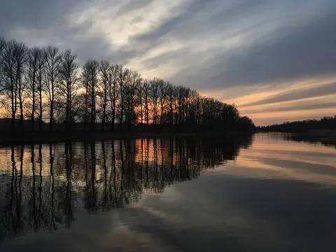 Sunset over river with trees and cloudy sky reflection Stock Photos