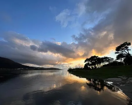 Sunset over river with trees and cloudy sky scene Stock Photos