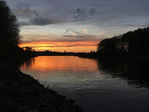 Sunset over river with trees and dark clouds in sky Stock Photos