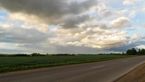 Sunset over the road between fields and meadows. Beautiful clouds. Horizontal Stock Photos