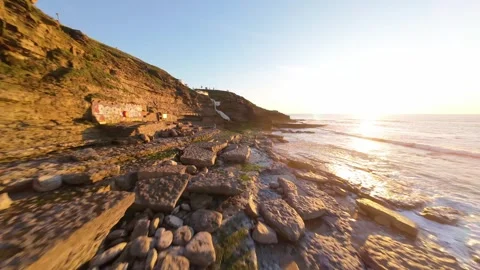 Sunset over rocky beach with gentle waves and distant swimmers Stock Footage 344558547