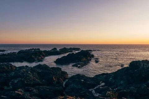 Sunset over rocky coastline with calm ocean waters Stock Photos