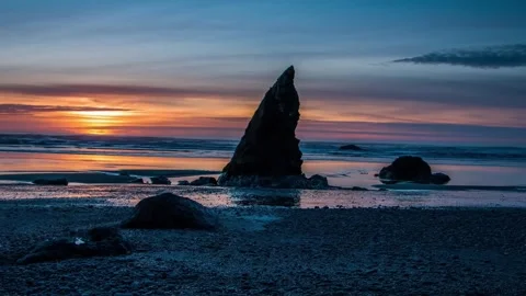 Sunset over rocky sea stack on coastal beach with reflection Stock Footage 342396161