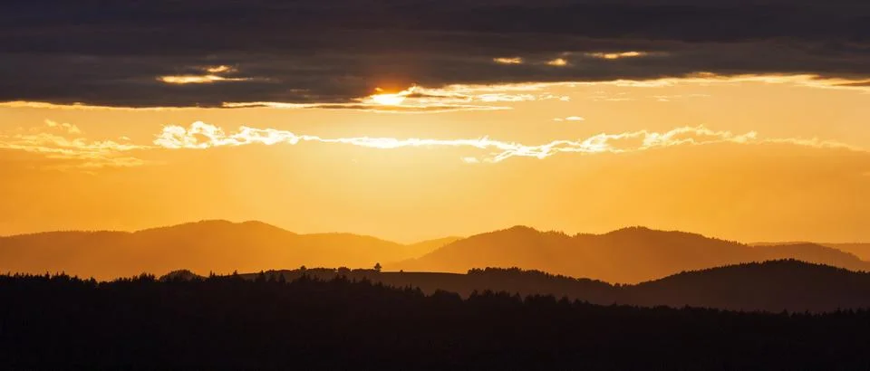 Sunset over rolling hills with a dramatic sky. Warm light casts long shadow.. Stock Photos