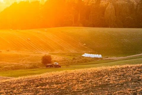 Sunset over rural fields with tractor and golden sunlight. Stock Photos