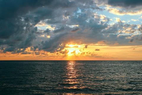 Sunset over the sea with dramatic clouds and sun reflection on water Stock Photos