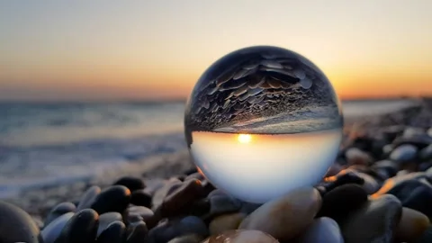 Sunset over the sea inverted inside a crystal lensball placed on a pebble beach. Stock Footage 335796781
