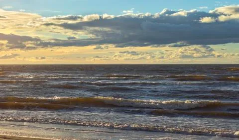 Sunset over the sea panorama in yellow and blue tones. Sea waves on the beach. Stock Photos