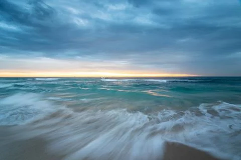 Sunset over the sea with rolling waves and overcast sky Stock Photos