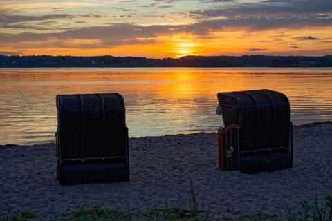Sunset over the sea with two beach chairs on sandy beach in Gluecksburg nea.. Stock Photos