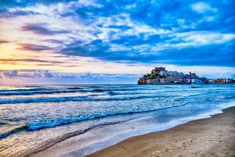 Sunset over shoreline with waves lapping against sandy beach and a coastal .. Stock Photos