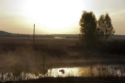 Sunset over a small lake in the middle of a foggy field Stock Photos