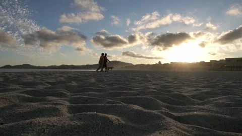 Sunset Over Textured Sandy Beach with Silhouetted People and Distant Hills in Stock Footage 345143301