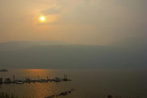 Sunset over the tranquil lake surrounded by mountains in smoky atmosphere d.. Stock Photos