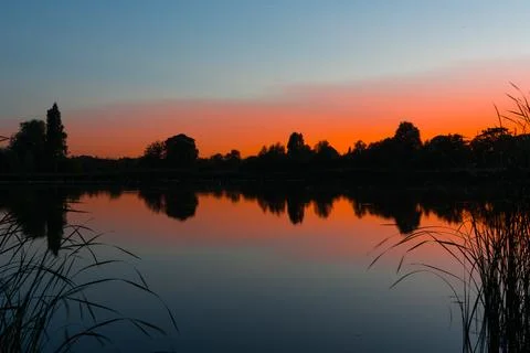 Sunset Over Tranquil Lake With Tree Silhouettes Stock Photos