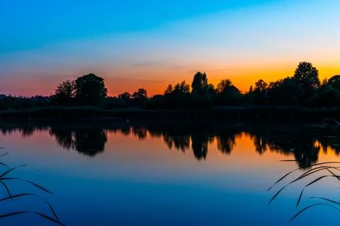 Sunset Over Tranquil Lake With Tree Silhouettes Stock Photos
