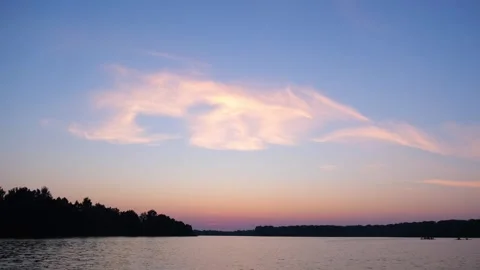 Sunset over a tranquil lake with wispy clouds. Serene landscape featuring a dark Stock Footage 340356773