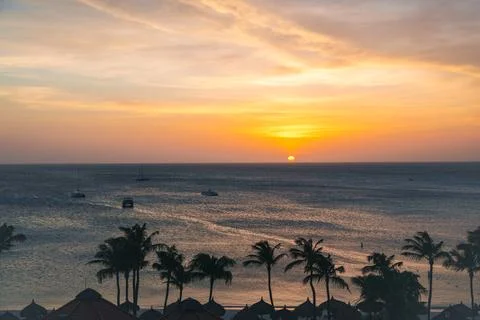 Sunset over tranquil ocean with palm trees and boats in peaceful coastal setting Stock Photos