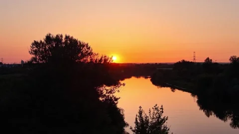 Sunset over a tranquil river with lush greenery and silhouettes of trees Vidéo 337911502