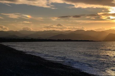 Sunset over tranquil waters with distant mountains and colorful clouds danc.. Stock Photos