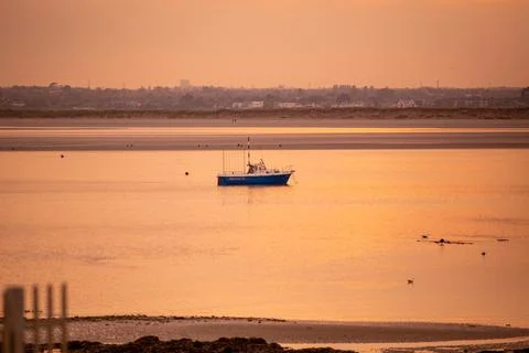 A Sunset Over Tranquil Waters Featuring a Small Fishing Boat Gliding Along Stock Photos